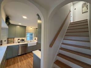 A kitchen with a wooden staircase, a coffee maker, and a sink.