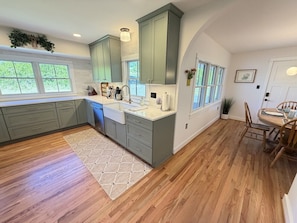 A kitchen with wooden floors, grey cabinets, a window, and a dining area with chairs.