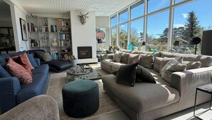 A spacious living room with a large window, a fireplace, and a bookshelf filled with books.