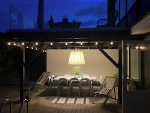 An outdoor dining area with a table and chairs, a lamp, and a view of the sky.
