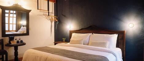 A neatly made bed with a wooden headboard, a bedside table with a lamp, and a mirror on the wall.