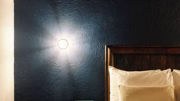 A bedroom with a dark wall, a wooden headboard, a bedside table with a microwave, and a bed with white bedding.