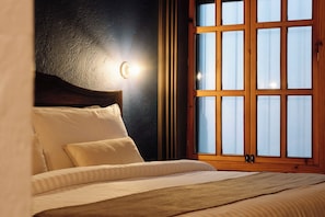Un letto con testiera, una lampada a parete e una finestra con tende.