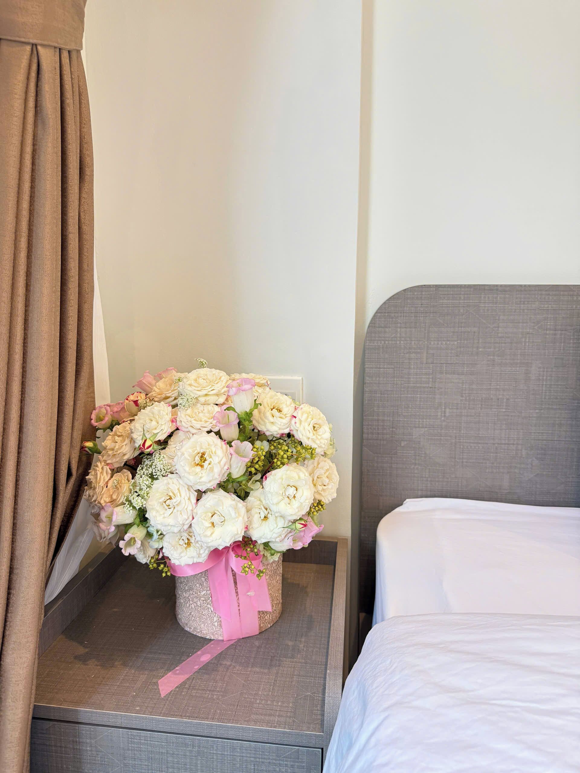 Una habitación de hotel con una cama, una mesita de noche con un ramo de flores y una cortina.