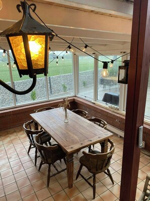 A dining area with a wooden table and chairs, a hanging lantern, and a view of a green field through large windows. - Soul in a 100-year-old villa on Langeland (Tranekær)