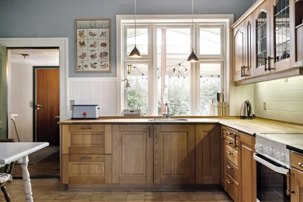 A kitchen with wooden cabinets, a large window, and a built-in oven. - Soul in a 100-year-old villa on Langeland (Tranekær)