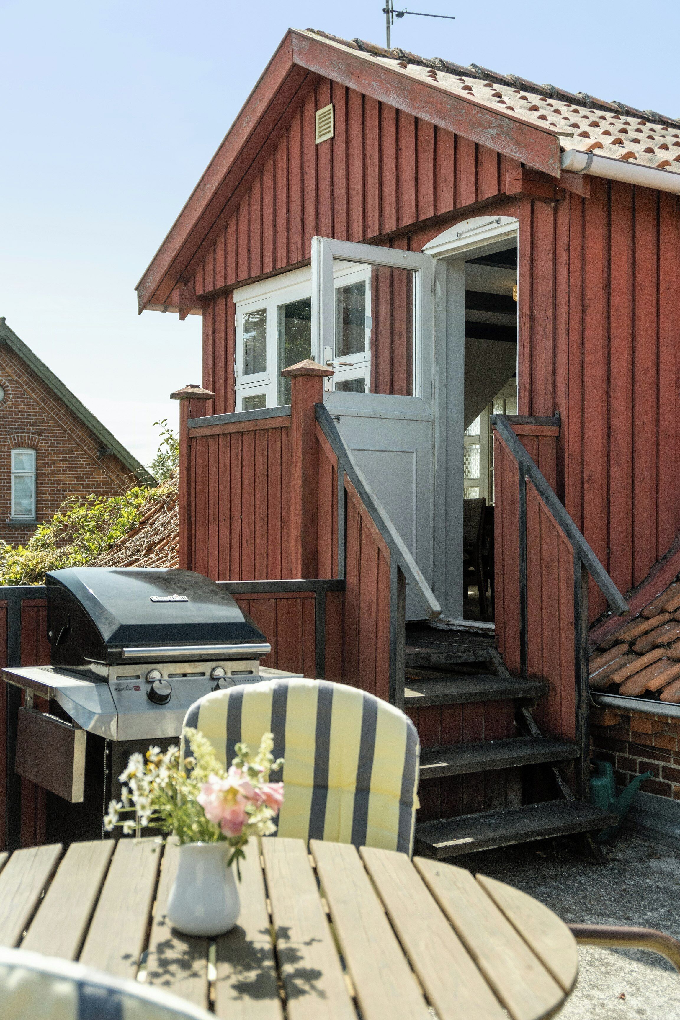 A wooden house with a red exterior, a front door, and a barbecue grill.
