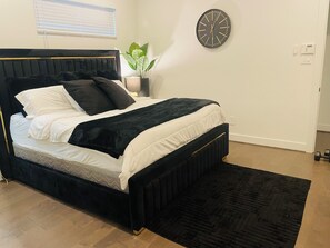 Un dormitorio con cama, un reloj de pared, una planta en maceta y una mesita de noche.