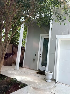 Una casa con fachada blanca, una puerta principal, un buzón y un árbol en primer plano.