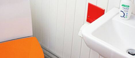 A bathroom with a white toilet, an orange seat, a sink with a bottle of hand soap, and a framed picture of Puerto Rico.