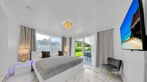 A modern bedroom with a large bed, a nightstand, a chair, and a TV.