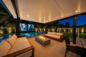 A modern outdoor living area with a pool, comfortable seating, and a large screen for entertainment.