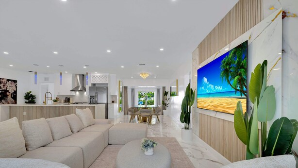 A modern living room with a sofa, ottoman, and a TV wall with a beach scene.