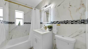 A bathroom with a bathtub, toilet, vanity, and a window.