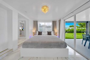 Una camera da letto moderna con un grande letto, un lampadario e vista su un prato verde attraverso ampie porte scorrevoli.