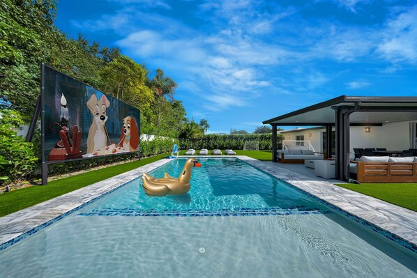 Une piscine agrémentée d’un cygne flottant, d’une fresque murale et d’un espace de détente extérieur moderne.