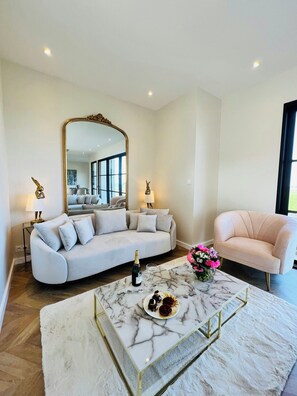 A modern living room with a white sofa, a pink armchair, a marble coffee table, and a large mirror. - Wellness villa with sea view in Brittany (Plouider)