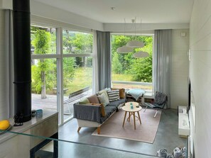 A modern living room with a sofa, a round table, and a large window offering a view of greenery. - Architect-house near Stenshuvud (Simrishamn)
