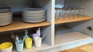 A kitchen cabinet with stacked plates, bowls, and utensils.