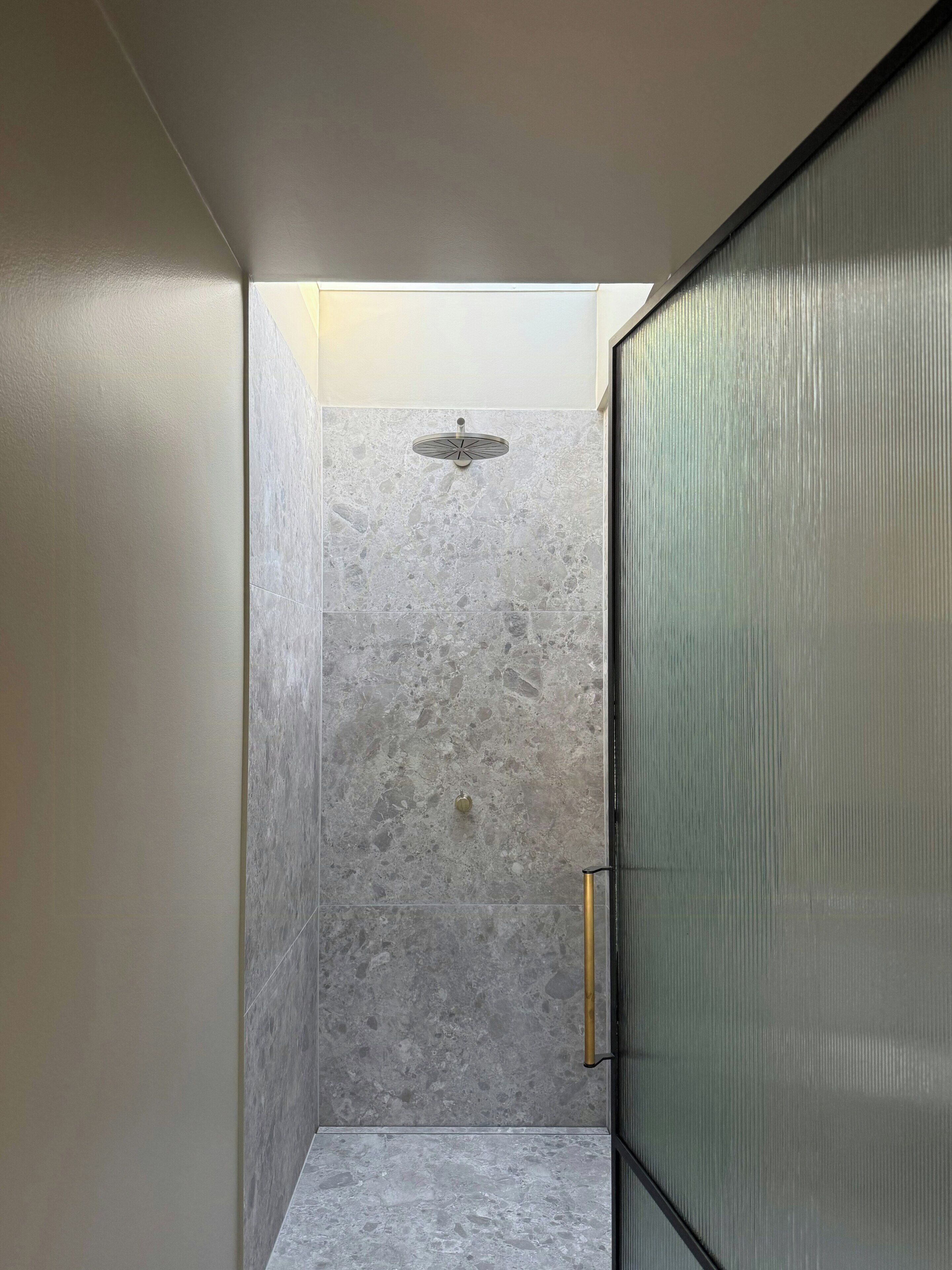 A shower with a glass door, a ceiling light fixture, and a textured wall.
