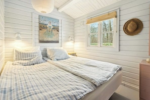 Ein Schlafzimmer mit einem Bett, zwei Nachttischlampen, einem Gemälde, einem Fenster mit Blick und einem Strohhut an der Wand.