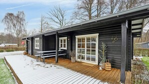 A black wooden cabin with a wooden deck, white windows, and a small outdoor seating area. - Comfortable summer house in Aabenraa (Aabenraa)