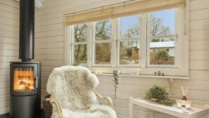 A cozy room with a wood-burning stove, a fluffy chair, a small round stool, and a white table with a plant and candles. - Comfortable summer house in Aabenraa (Aabenraa)