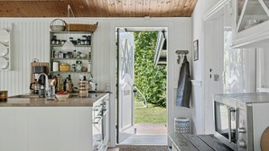 Una cocina con muebles blancos, techo de madera y vista a un jardín a través de una puerta abierta.