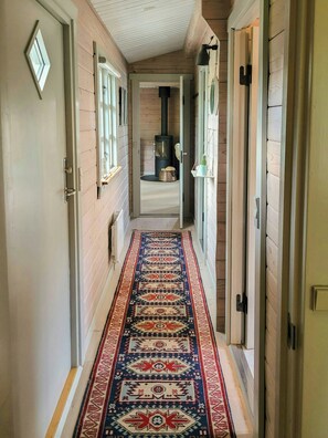 A hallway with a patterned rug, wooden walls, and a black stove.