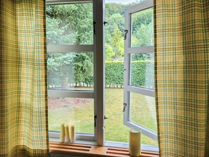 A window with a view of a garden, curtains, and a wooden shelf with candles.