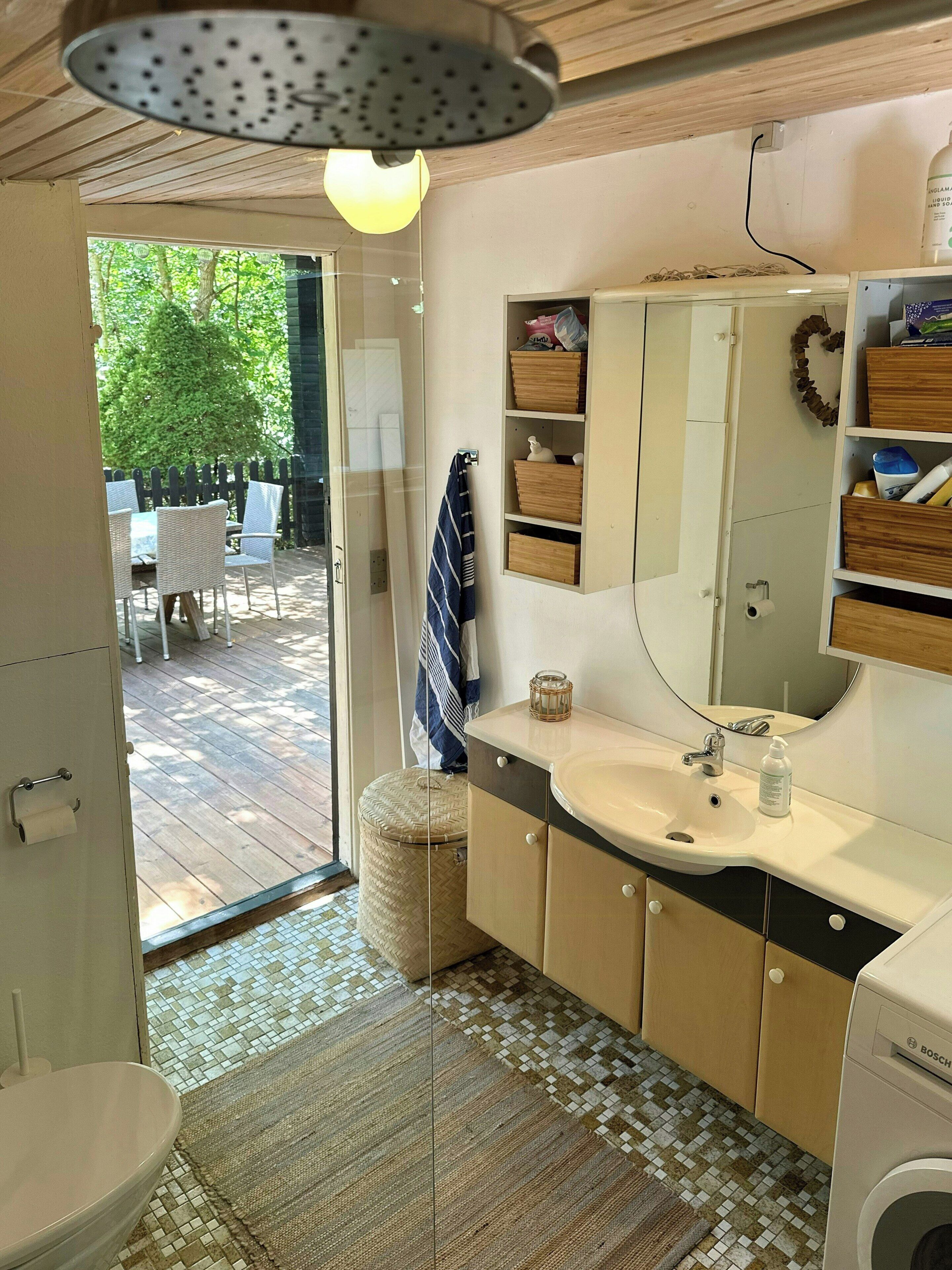 Une salle de bain avec un lavabo, un miroir et des toilettes. On y trouve un tabouret en osier et un porte-serviettes.