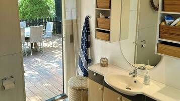 Une salle de bain avec un lavabo, un miroir et des toilettes. On y trouve un tabouret en osier et un porte-serviettes.