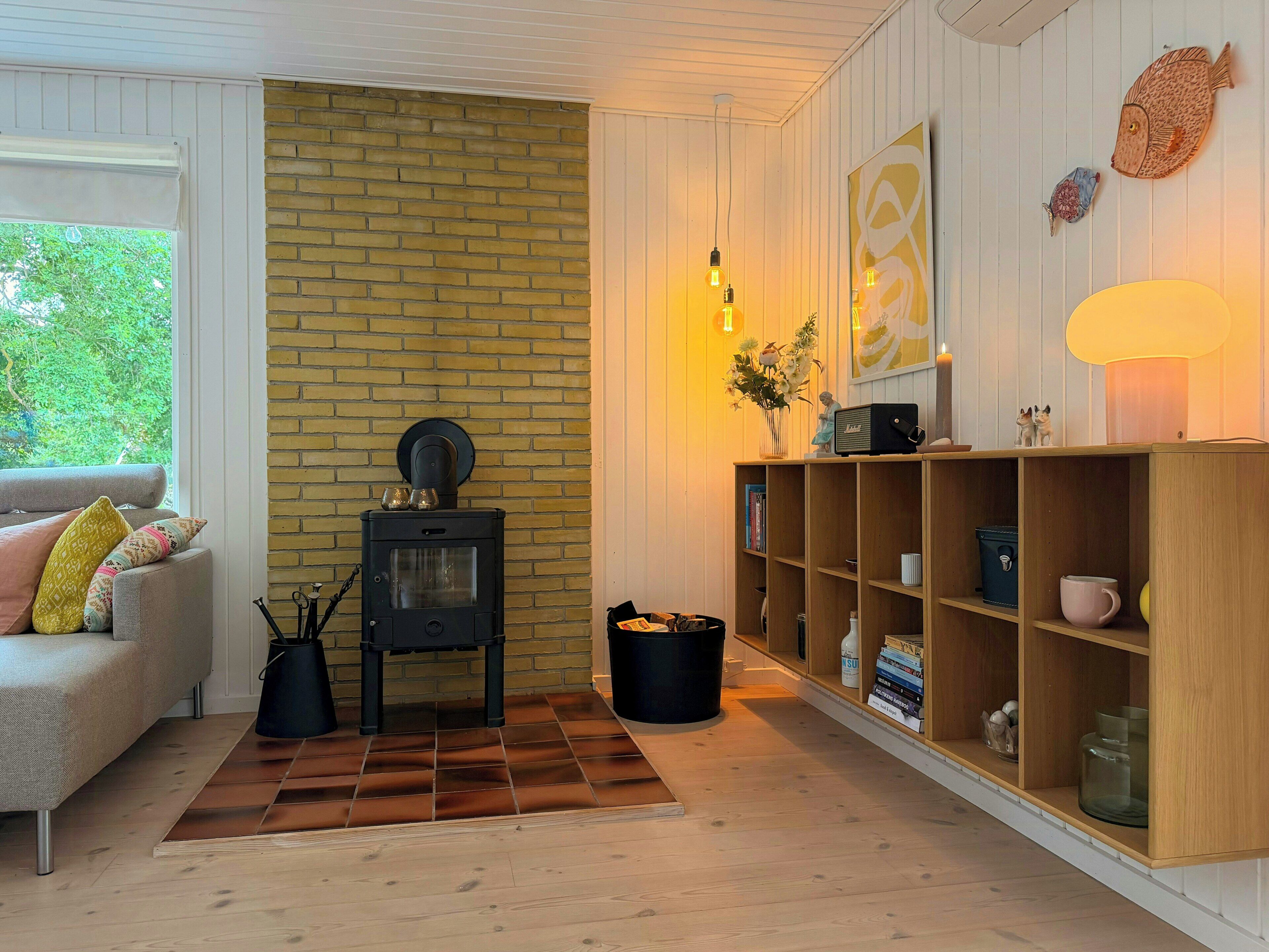 Una sala de estar acogedora con pared de ladrillo, un sofá con cojines, una estantería de madera y una chimenea.