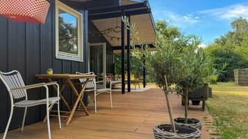 Terraza de madera con mobiliario exterior, un bolso colgado y plantas en macetas.