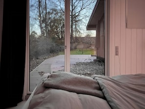 Ein Schlafzimmer mit großem Fenster, einem Bett und Blick auf eine Auffahrt und Bäume.