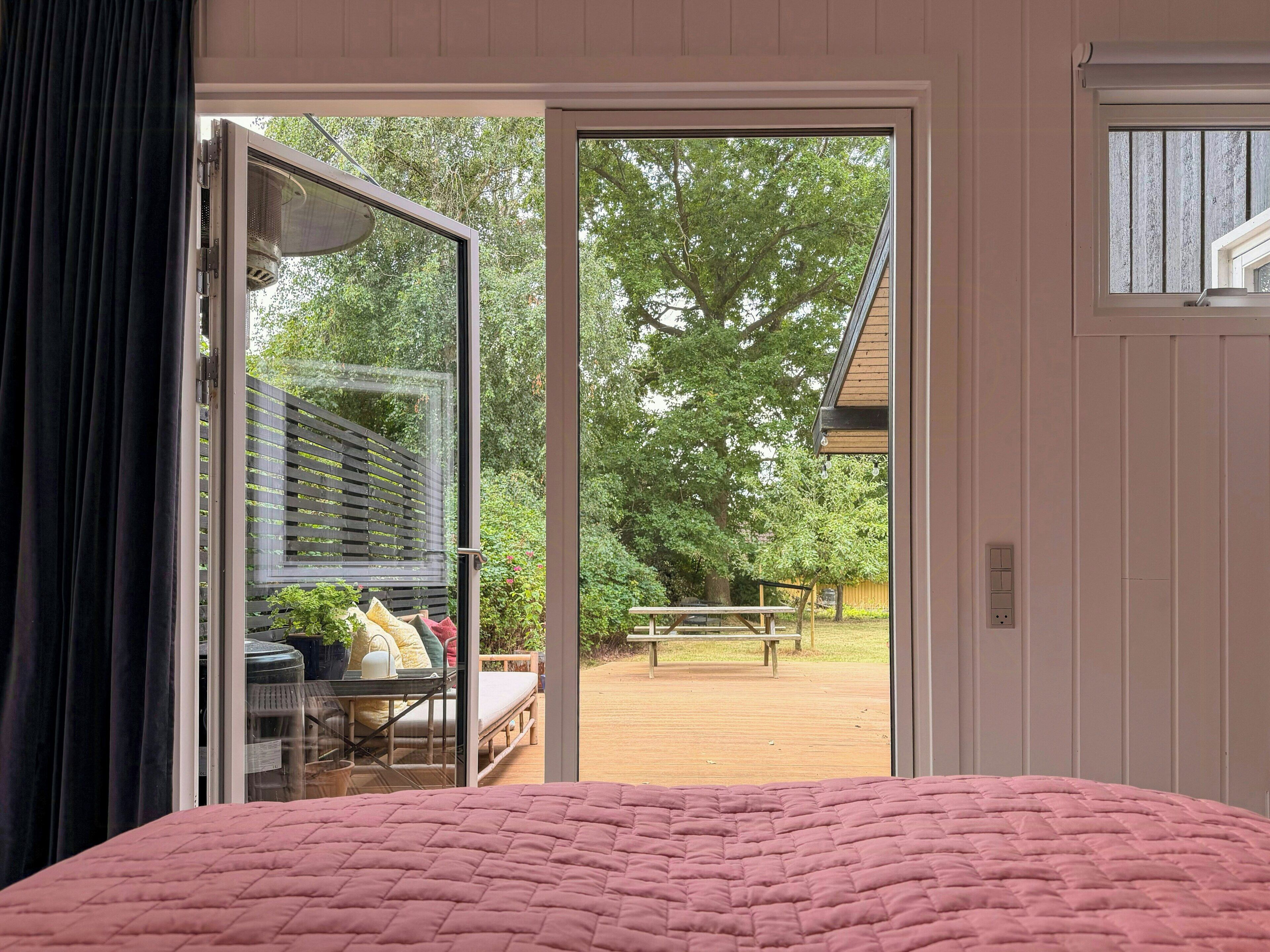 A bedroom with a large bed, a sliding glass door leading to an outdoor patio area with a wooden deck and a bench.