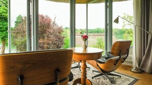 A room with a wooden ceiling, large windows, a wooden chair, a small table, and a vase with flowers. - Apartment in a thatched cottage with private lake (Grebin)