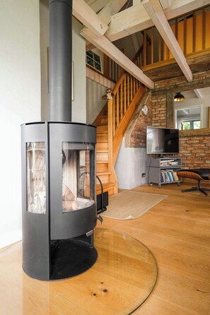 A modern living room with a wood-burning stove, a television, and a staircase. - Apartment in a thatched cottage with private lake (Grebin)
