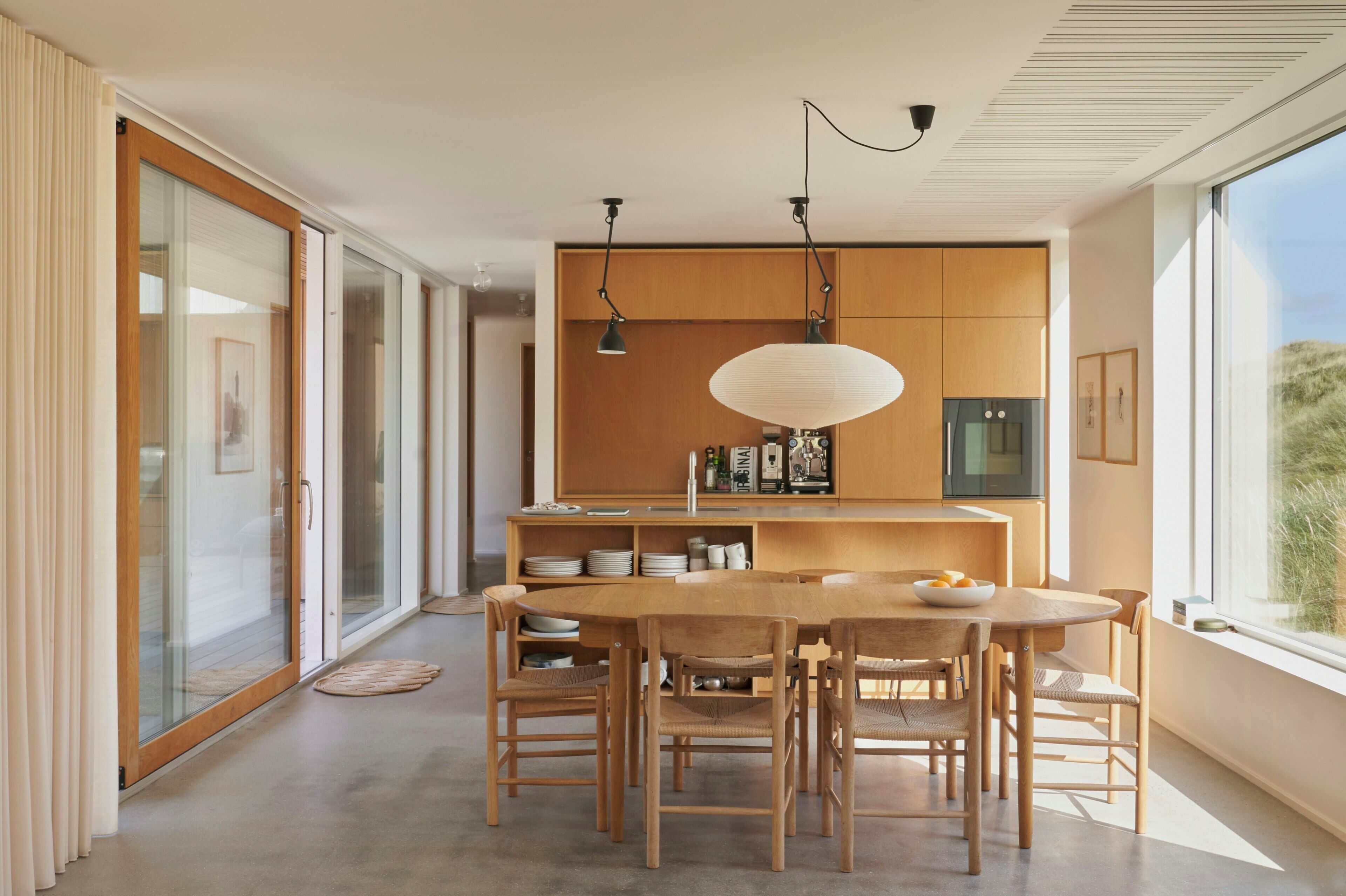 Une cuisine moderne avec des meubles en bois, une table à manger avec des chaises et des luminaires suspendus.