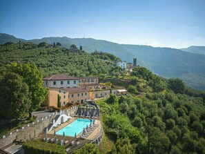 Ein Hotel an einem Hang mit Schwimmbad, terrassenförmigen Gärten und einer Kirche auf einem Hügel.