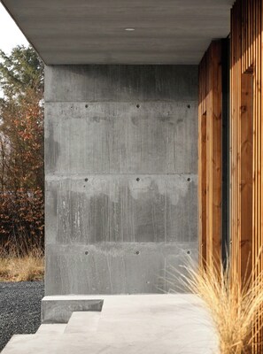 A concrete exterior wall with a wooden door frame, a concrete step leading to the entrance, and a gravel driveway. - Hotel vibe in architectural settings (Årre)