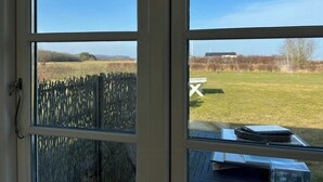 A view through a window with a wooden fence, a picnic table, and a building in the distance. - House in peaceful surroundings 150 m to the water (Asperup)