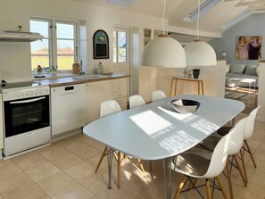 Une cuisine moderne équipée d’un four Beko, d’un évier et d’un coin repas avec une table et des chaises blanches.