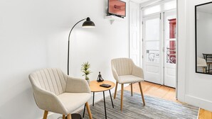 A modern room with two armchairs, a small table, a floor lamp, and a television displaying 'GUEST READY'.
