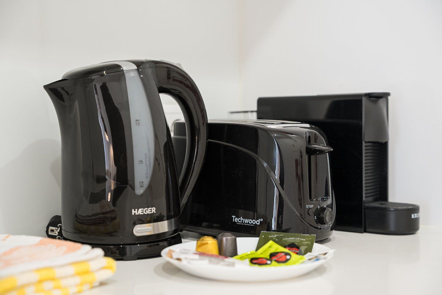 Een keuken met een zwarte HEGER waterkoker, een zwarte Techwood koffiezetapparaat en een bord met etenswaren.