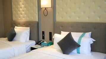 A hotel room with two beds, a wall-mounted light, a control panel, and a bedside table with a phone and a tissue box.