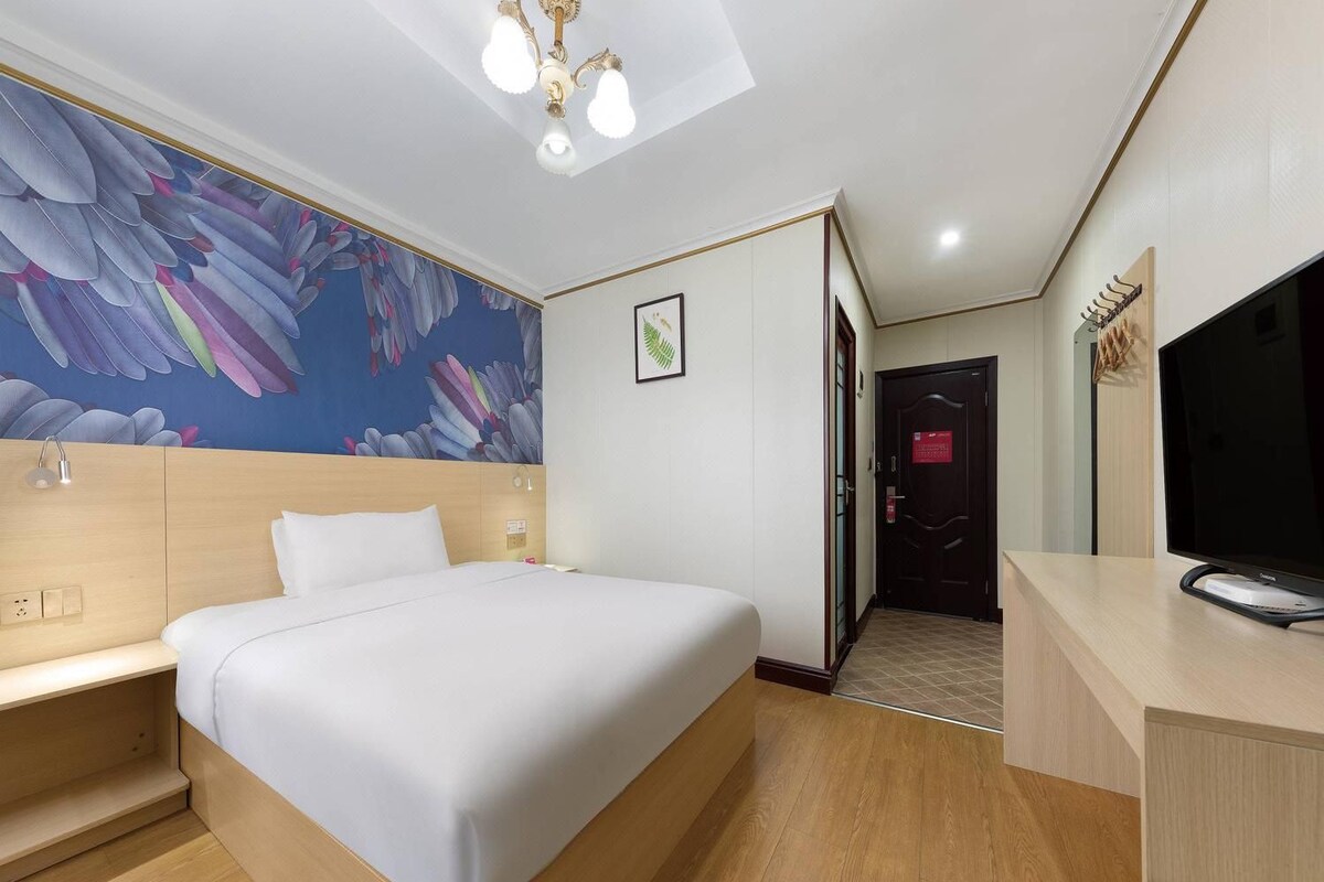 A hotel room with a bed, a desk, a television, and a mural on the wall.