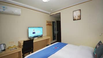 A hotel room with a bed, a desk with a computer, a mirror, and a wall-mounted air conditioner.