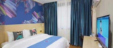 Habitación de hotel con cama, escritorio, televisor, ventilador de techo y un mural floral en la pared.