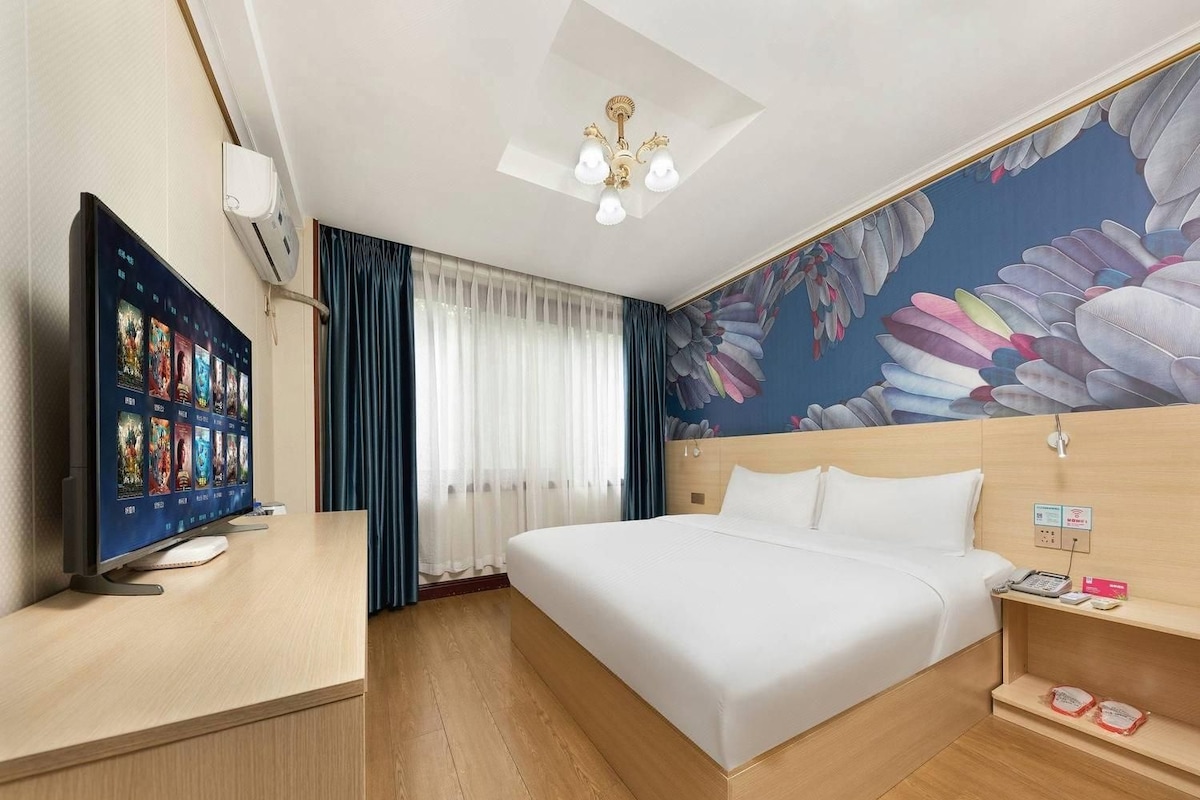 A hotel room with a bed, a TV, a desk, and a wall with a floral mural.